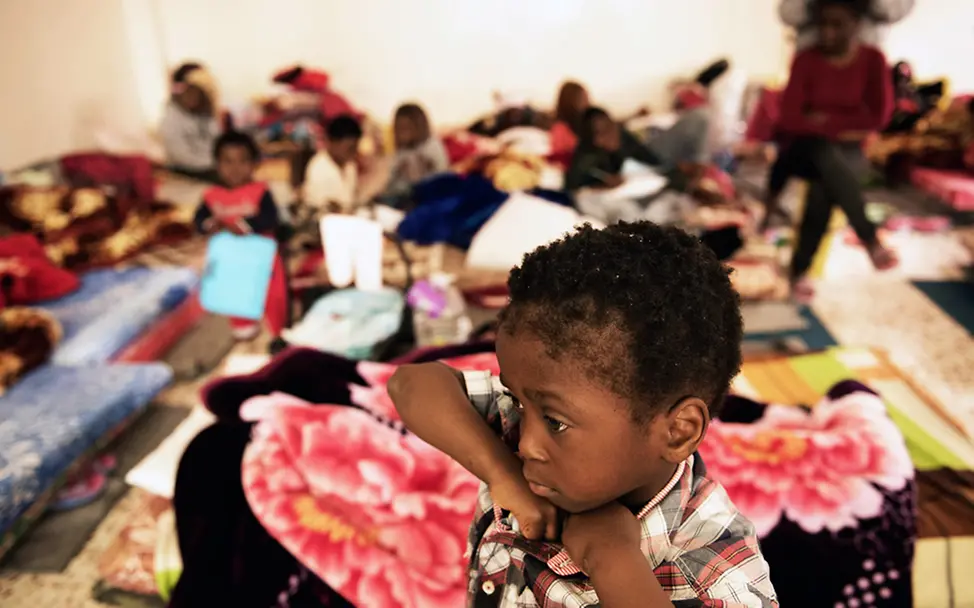 Ein kleiner Jugne steht inmitten von Matratzen. Hier schlafen und leben Menschen auf engstem Raum. | © UNICEF/Romenzi Ein kleiner Jugne steht inmitten von Matratzen.