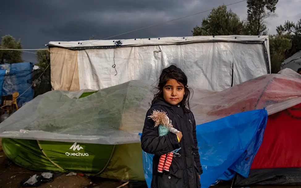 Leben auf der Flucht bedeutet Leben im Zelt. | © UNICEF/Haviv VII Photo UN-Kinderrechtskonvention: Ein junges Mädchen mit einer Puppe im Arm vor einem Zeltlager.