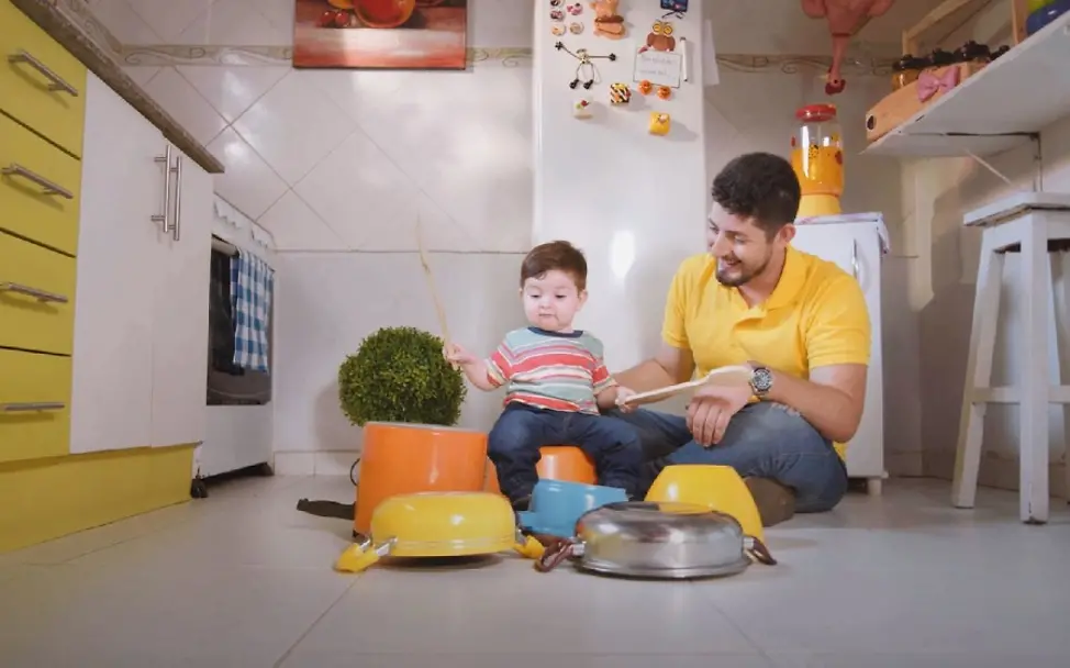 Vater bringt Sohn auf Töpfen das Schlagzeugspielen bei. | © UNICEF/Rai Kinder und Musik: Vater und Sohn spielen auf Töpfen Schlagzeug.