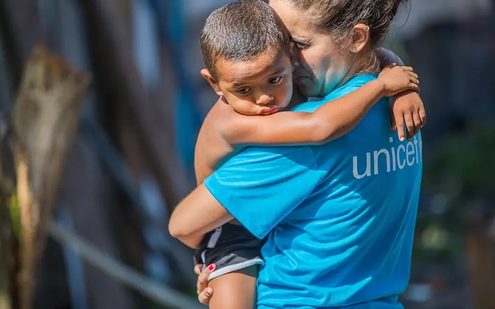 Viele Kinder sind in Krisenzeiten völlig allein. | © UNICEF/Libório Brasilien: Eine UNICEF-Mitarbeiterin hält einen kleinen Jungen im Arm.