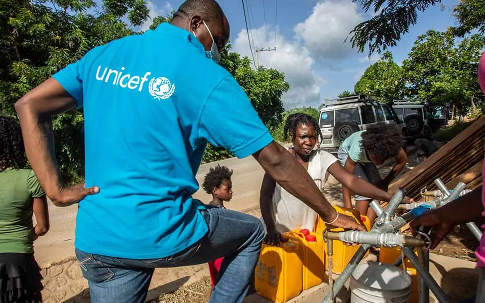 UNICEF richtet Wasserstationen ein und liefert in Wassertrucks sauberes Trinkwasser. | © UNICEF/Rouzier Haiti Erdbeben Nothilfe: Ein UNICEF-Mitarbeiter hilft beim Befüllen von Wasserkanistern.