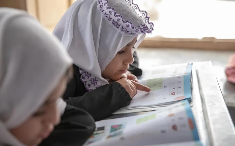 Afghanistan: Zwei Mädchen schauen auf ein Lernbuch.