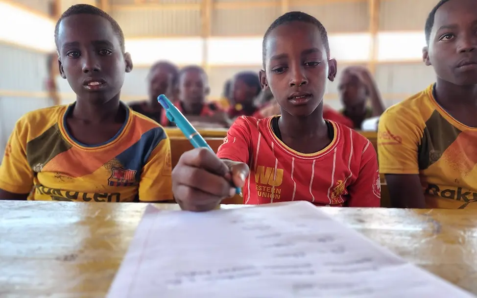 Wie Kinder trotz Klimakrise weiterlernen I UNICEF Somalia/Mumin Somali: Adan sitzt neben seinen Klassenkameraden an einem Tisch und schreibt.