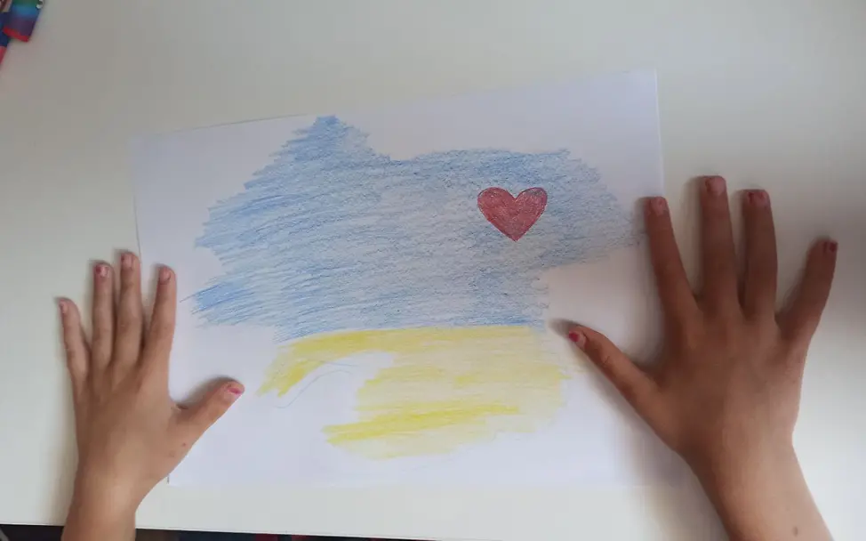 Ein Mädchen zeigt das Bild einer Ukraine-Flagge mit Herz, das sie gemalt hat. | © UNICEF/UNICEF Ukraine Zerstörter Kachowka-Staudamm: UNICEF erreichtet Kinderschutzzentren als Anlaufstellen für evakuierte Kinder.