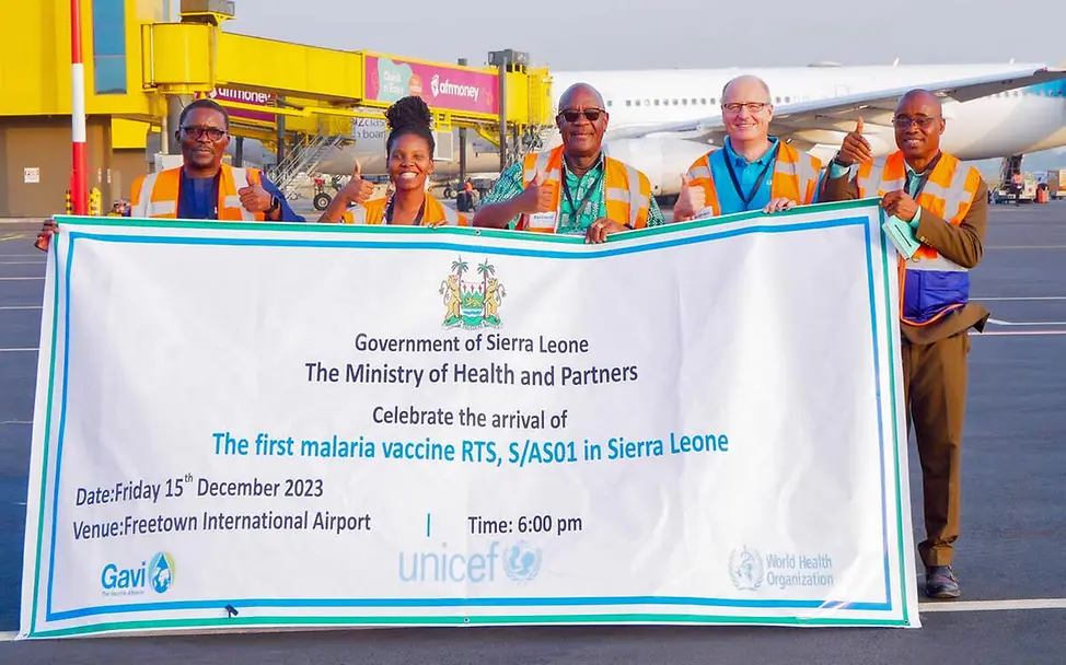 Malaria-Impfstoff kommt in Sierra Leone am Flughafen an | © UNICEF/Mansaray Fünf Menschen halten einen Banner hoch, auf dem die Ankunft der ersten WHO zugelassenen Malaria-Impfstoffe angekündigt wird.
