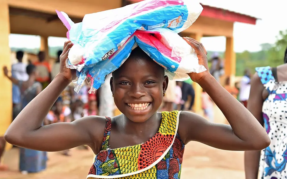 Malaria: UNICEF hilft Kindern im Kampf gegen die Infektionskrankheit. | © UNICEF/Dejongh Ein Mädchen in der Elfenbeinküste trägt mehrere Päckchen Moskitonetze nach Hause.
