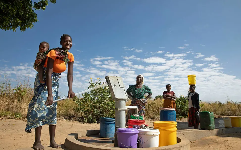 Sambia: Frauen stehen an einer Wasserstelle an, um sauberes Trinkwasser zu pumpen | © UNICEF/Schermbrucker Sambia Wasser: Eine Frau pumpt an einer Wasserstelle Wasser in einen Eimer.