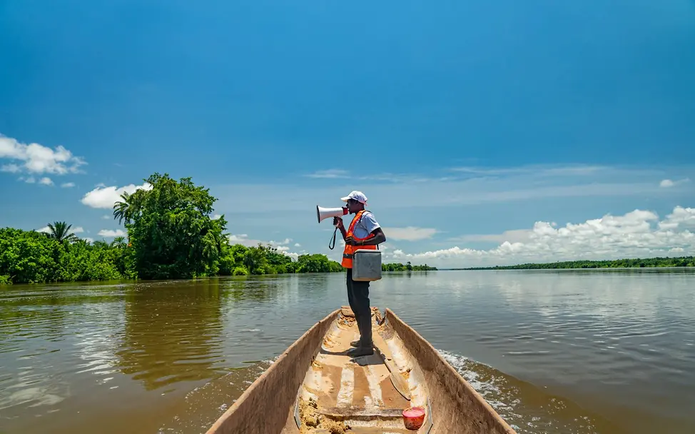 Ein Mann ruft in ein Megafon auf einem Boot in Tansania. I © UNICEF/Mulala Tansania: Ein Impfhelfer informiert Eltern, dass sie ihre Kinder impfen lassen können.