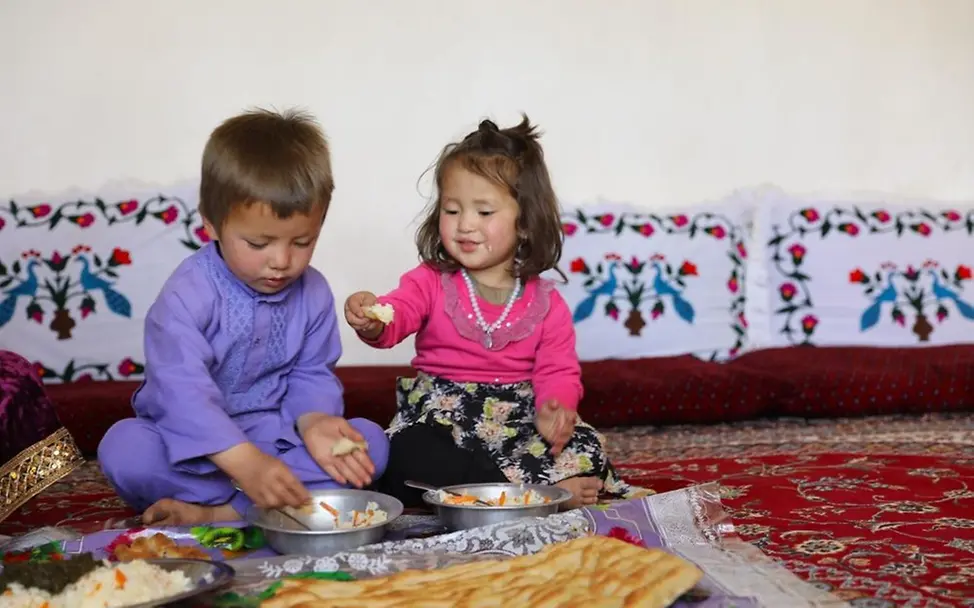 Zwei Kinder probieren das Essen, das ihre Mutter für sie gekocht hat. | © UNICEF/UNI827357/ Afghanistan: Zwei Kinder essen gemeinsam zu Mittag.