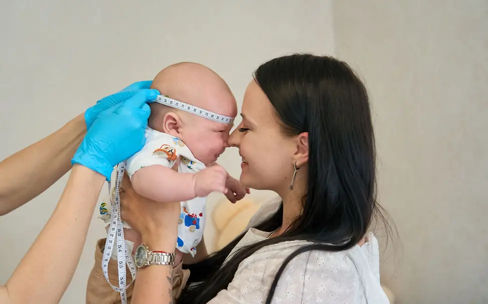Ukraine: Eine Mutter hält ihr Baby, während ihm der Kopfumfang gemessen wird. I © UNICEF/UNI414276/Vashkiv Einem Baby wird der Kopfumfang gemessen. Die Menschen in der Ukraine benötigen Hilfsgüter.