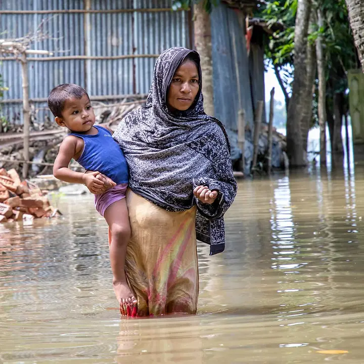 Monsun in Asien: Eine Mutter in Bangladesch trägt ihr Kind durch hüfthohes Wasser. 