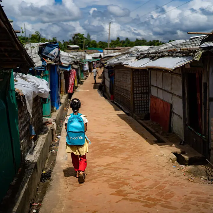 Rohingya Flüchtlingslager: Ein Mädchen mit UNICEF-Schulrucksack läuft zwischen Hütten im Rohingya-Camp entlang.