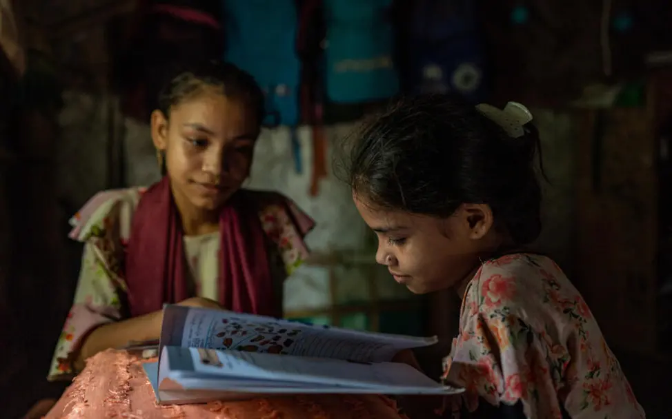 Rohingya Flüchtlingslager: Zwei Mädchen sitzen mit einem Schulbuch in ihrer Unterkunft.  