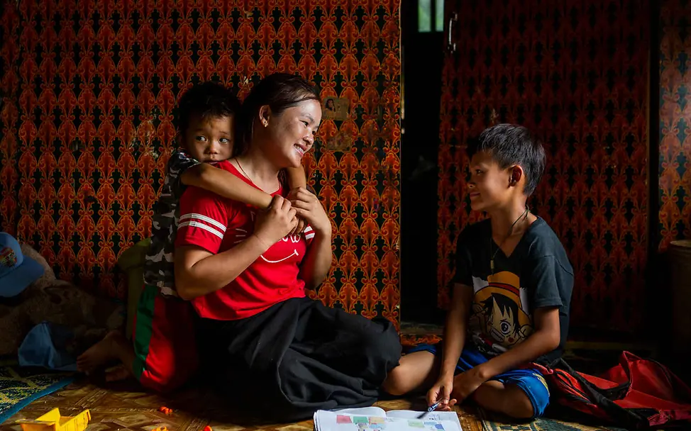 Menschenrechte einfach erklärt: Eine Mutter sitzt mit ihren zwei Kindern auf dem Boden ihres Hauses.