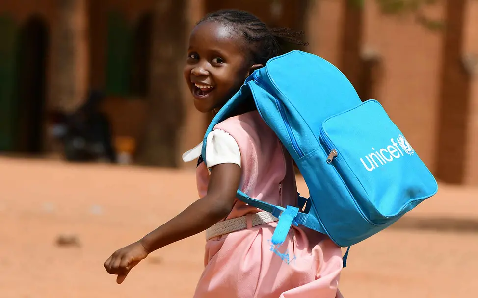 Menschenrechte einfach erklärt: Ein Mädchen mit einem UNICEF-Schulrucksack blickt lachend über die Schulter.