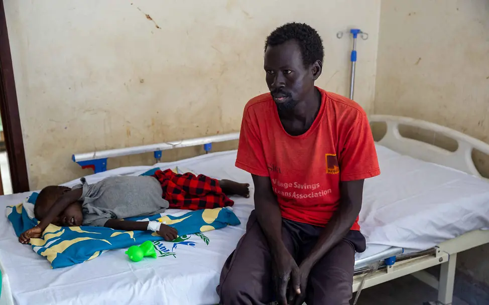 Südsudan Hungerkrise: Ein Vater sitzt bei seinem Kind auf einem Krankenhausbett.