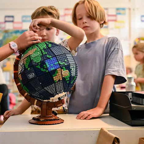 Klimaschutz einfach erklärt: Kinder schauen sich eine Weltkugel aus Legosteinen an.