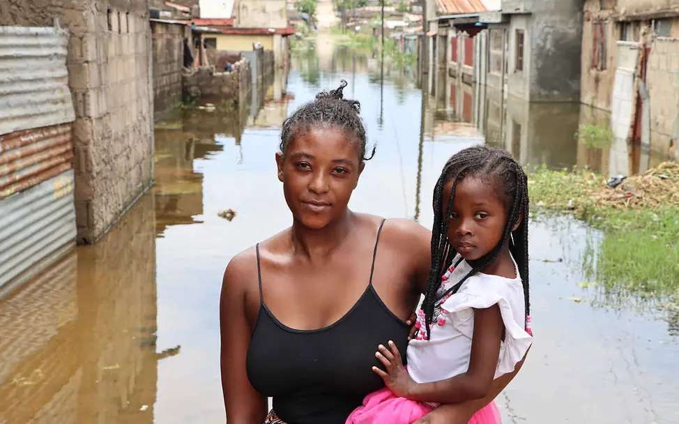 Klimaschutz einfach erklärt: Eine Mutter steht mit ihrer Tochter auf dem Arm in einer überschwemmten Straße.