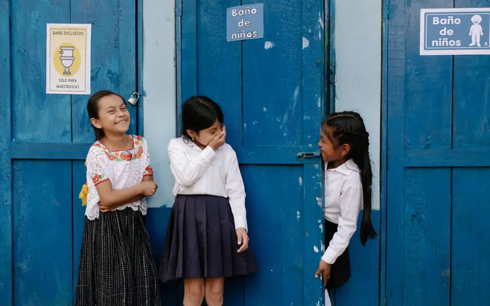 Sauberes Wasser: Drei Mädchen stehen lachend vor Toilettenhäuschen.