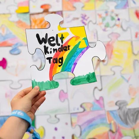 Weltkindertag einfach erklärt: Eine Kinderhand hält ein gemaltes Puzzleteil.