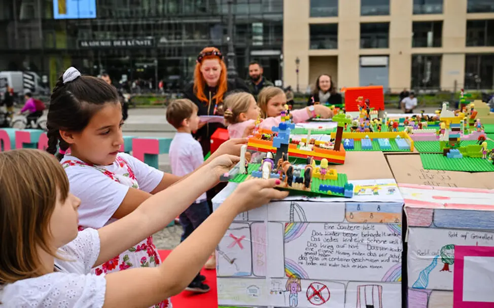 Weltkindertag einfach erklärt: Kinder präsentieren ihre Bauwerke aus Lego.  