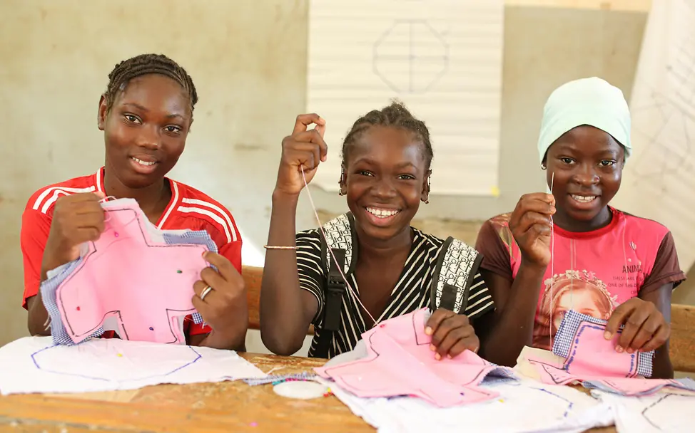 Was ist Periodenarmut: Drei Mädchen nähen Stoffbinden.