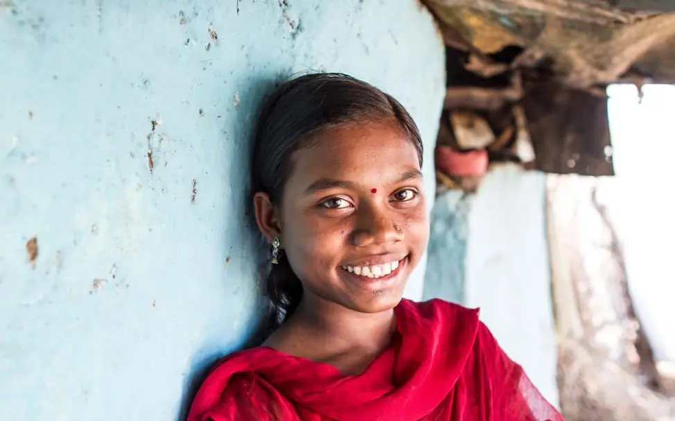Kinderarbeit Indien: Ein Mädchen kann dank UNICEF und Nichtregierungsorganisationen wieder zur Schule gehen. | © UNICEF India /Singh Die 14-jährige Vaishali lehnt lächelnd an einer blauen Wand.